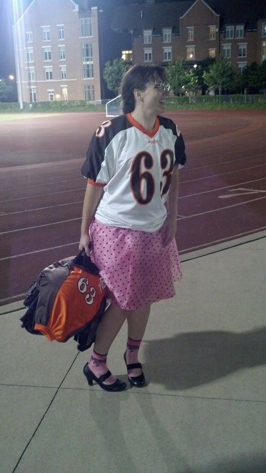 Marie wearing a pink party dress and football jersey, carrying her shoulder pads
