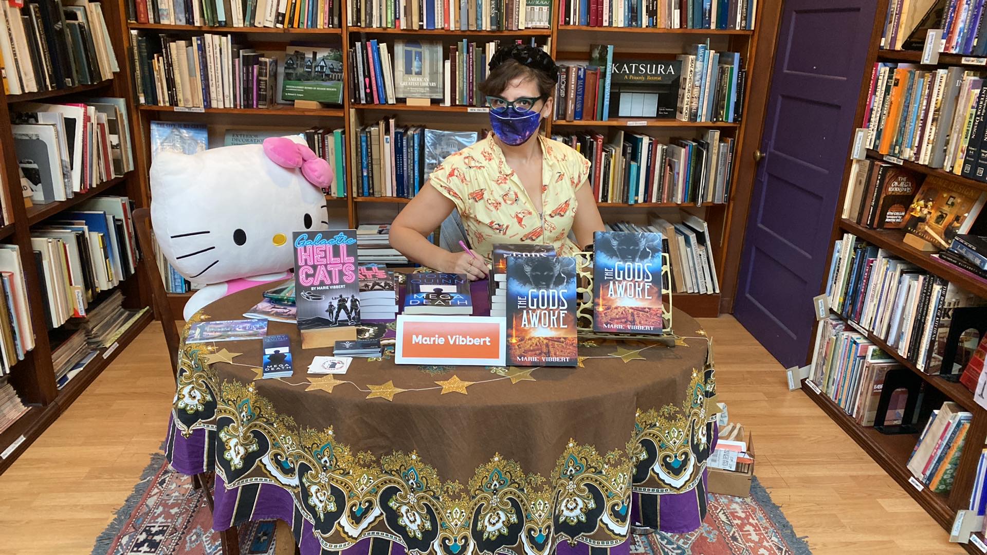 Marie sits at a signing table in a bookstore with a giant hello kitty next to her