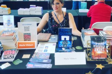 Smiling white lady behind a table full of books.