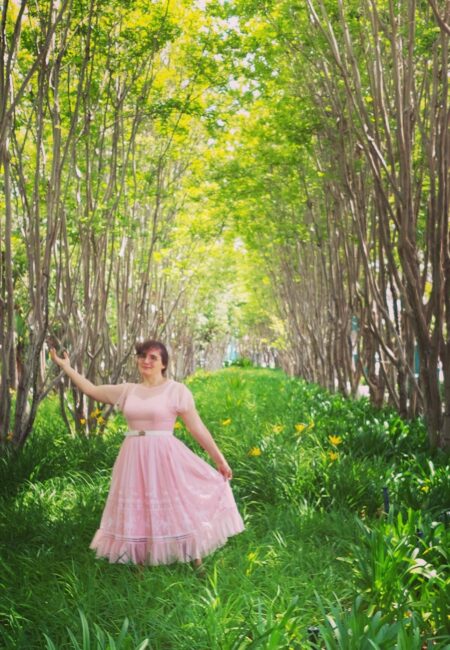 Woman in pink frilly dress poses dramatically in a forest glade