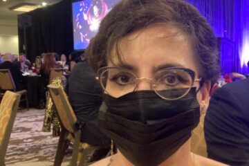 woman in evening attire wearing mask with ballroom and lighted stage behind her