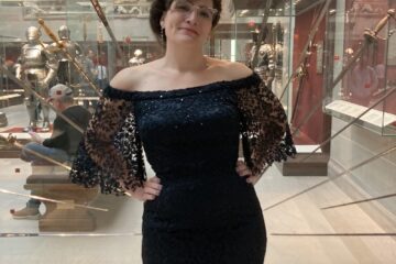 Woman in evening gown stands in front of display case of swords