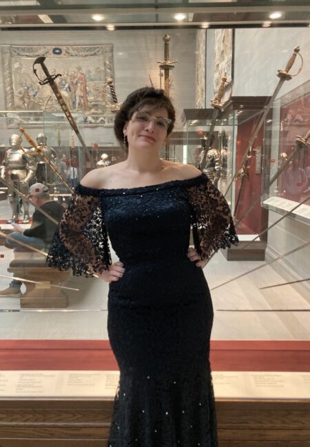 Woman in evening gown stands in front of display case of swords