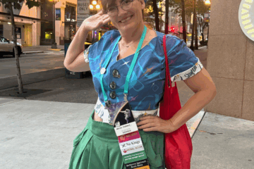Woman in blue headscarf and 1950s shirt-blouse posing for a portrait on a quiet streetcorner at dusk